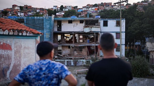 48-летний Хесус Линарес стоит рядом с местным жителем, который смотрит на свой жилой дом, поврежденный ударом США, в Катиа-ла-Мар, Венесуэла, 4 января 2026 года. (Фото Gaby Oraa / Reuters)