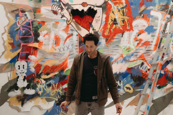 Эдриен Броуди на фоне одной из своих картин (Whitehot)